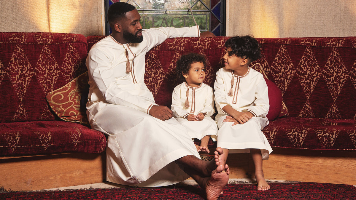 A man and three children wearing cream CAVE thobes, seated together indoors